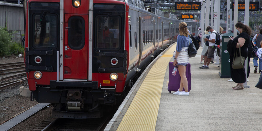 Image of a people waiting for a train in New Haven. Several people wait on the platform while a train slowly arrives.