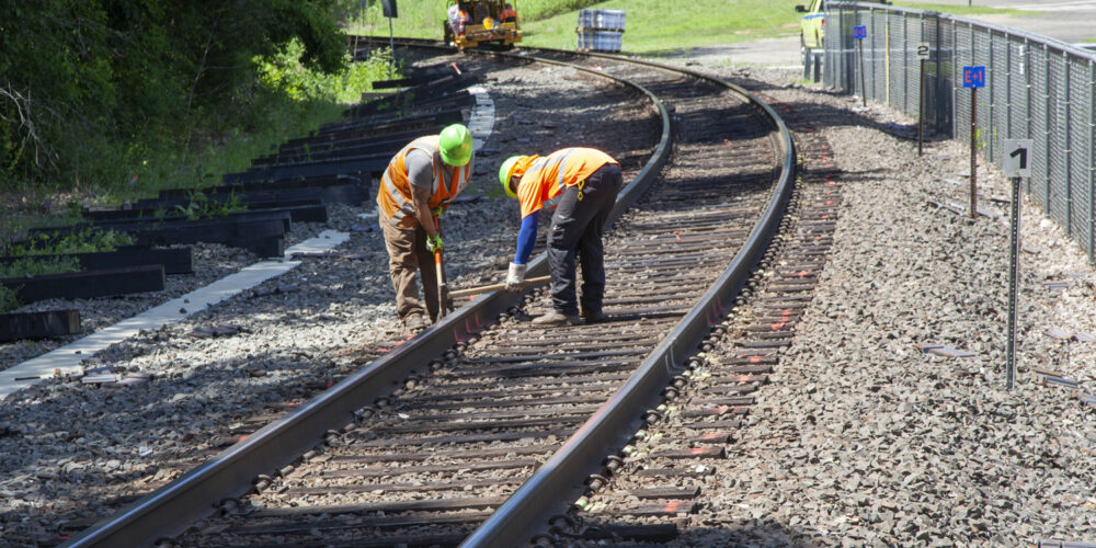 Construction at Beacon Falls Station. There are two workers hammering railroad tracks.
