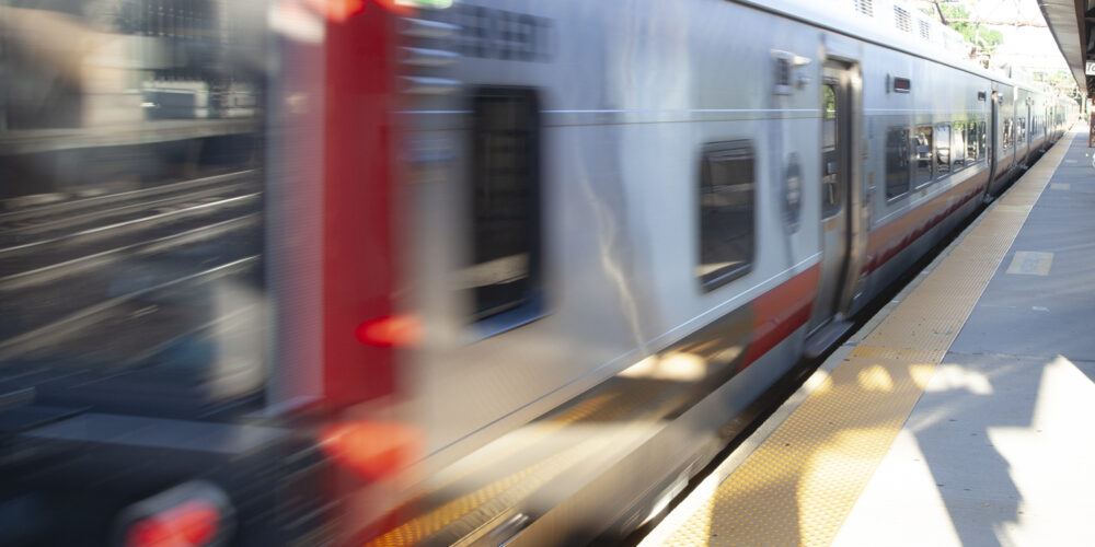 M8 train in motion leaving station in Greenwich. The foreground is blurry and nobody is waiting on the platform.